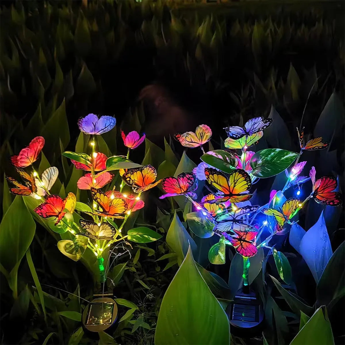 Farfalle solari accese in giardino di notte, LED colorati tra le foglie